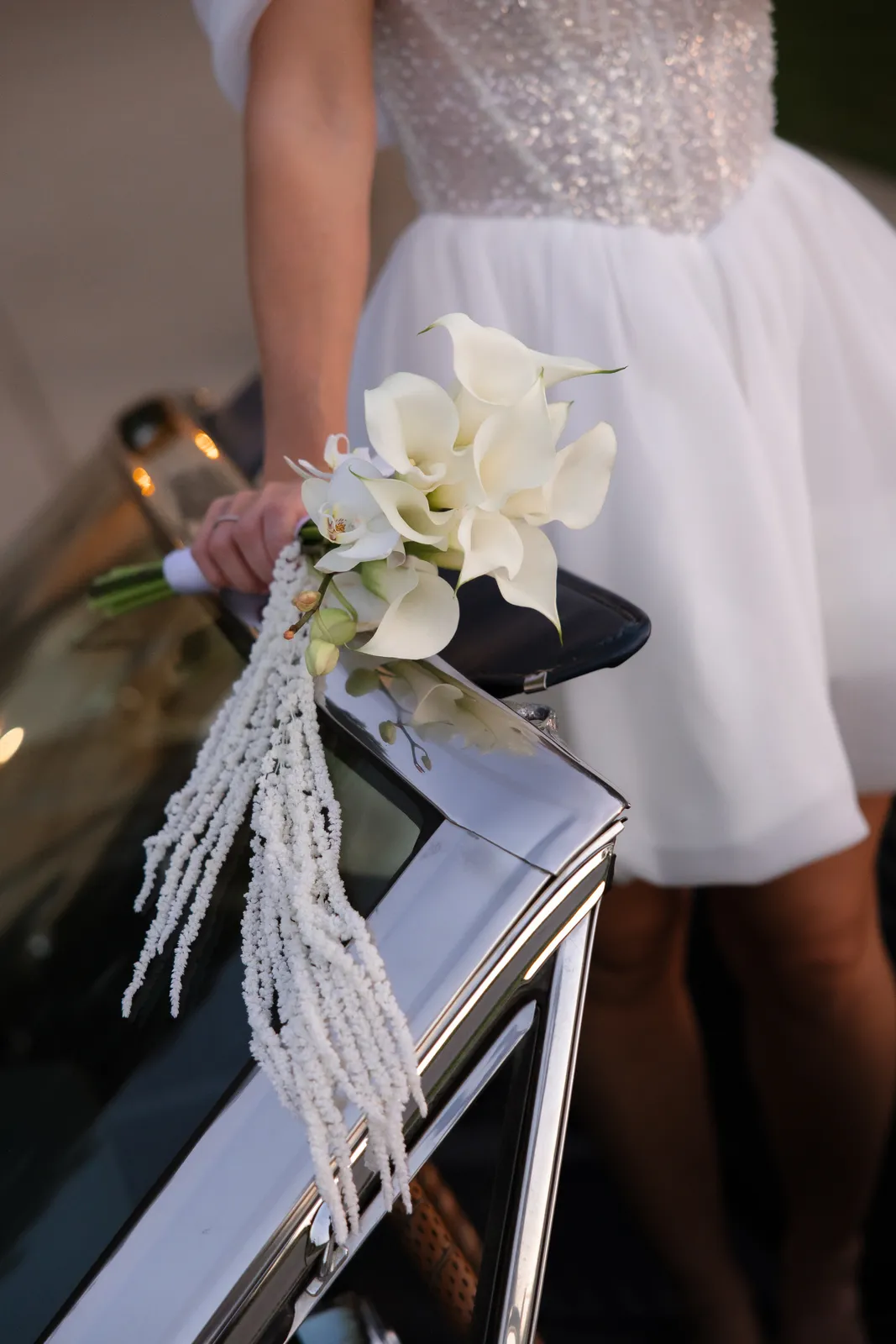 Calla lily bouquet held against a white vintage car