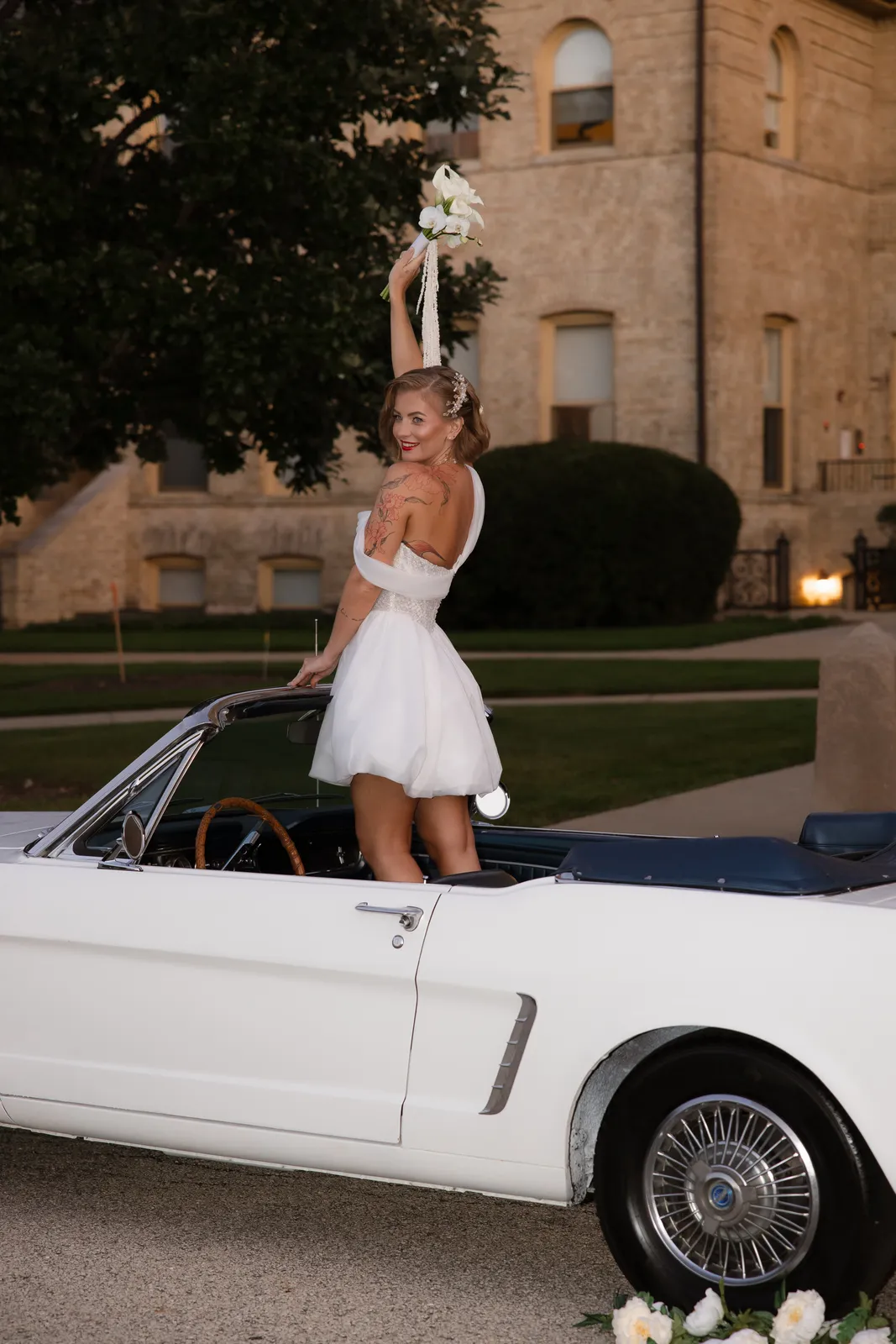 Bride standing in a vintage convertible, bouquet raised