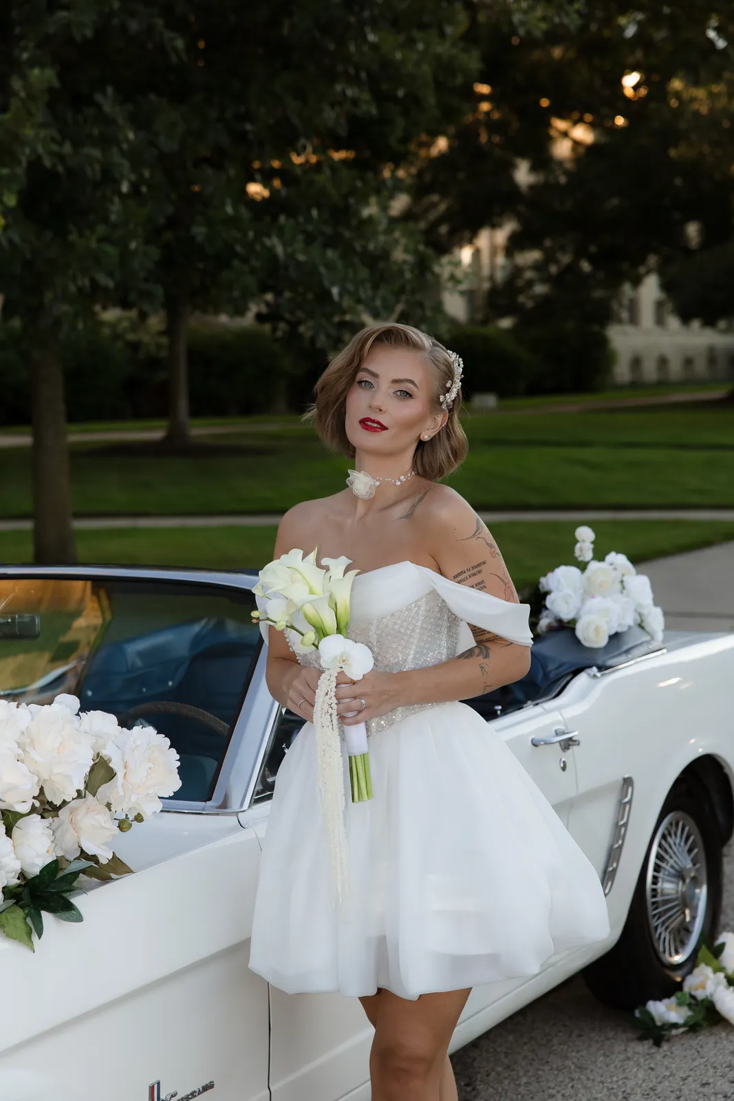 Bride with a pearl hair piece and bold red lip beside a white convertible