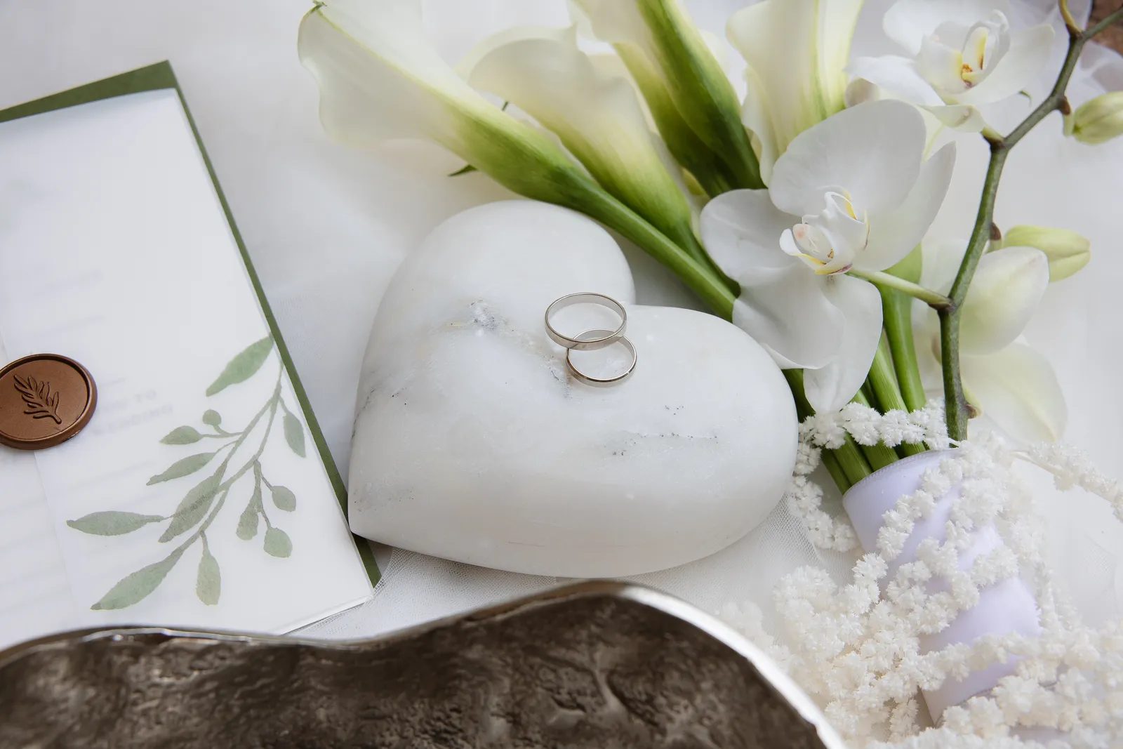 Wedding rings on a marble heart with calla lilies and orchids