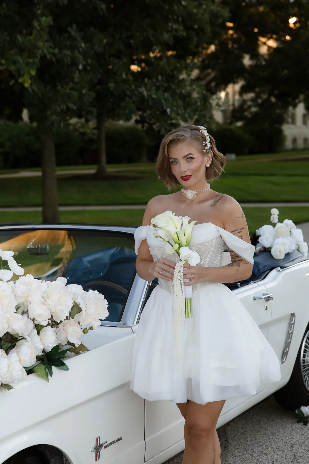 Bride with a short textured bob, red lip and calla lily bouquet by a vintage car