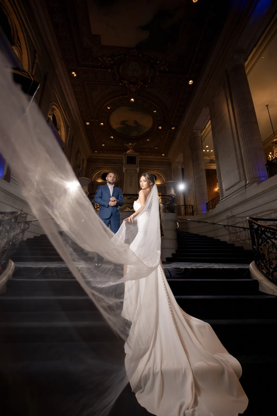 Couple on a sweeping staircase, the bride's veil in motion