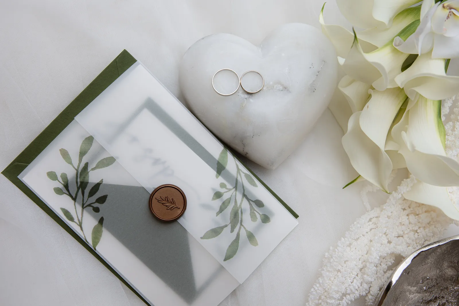 Wedding rings on a marble heart beside an invitation with a wax seal
